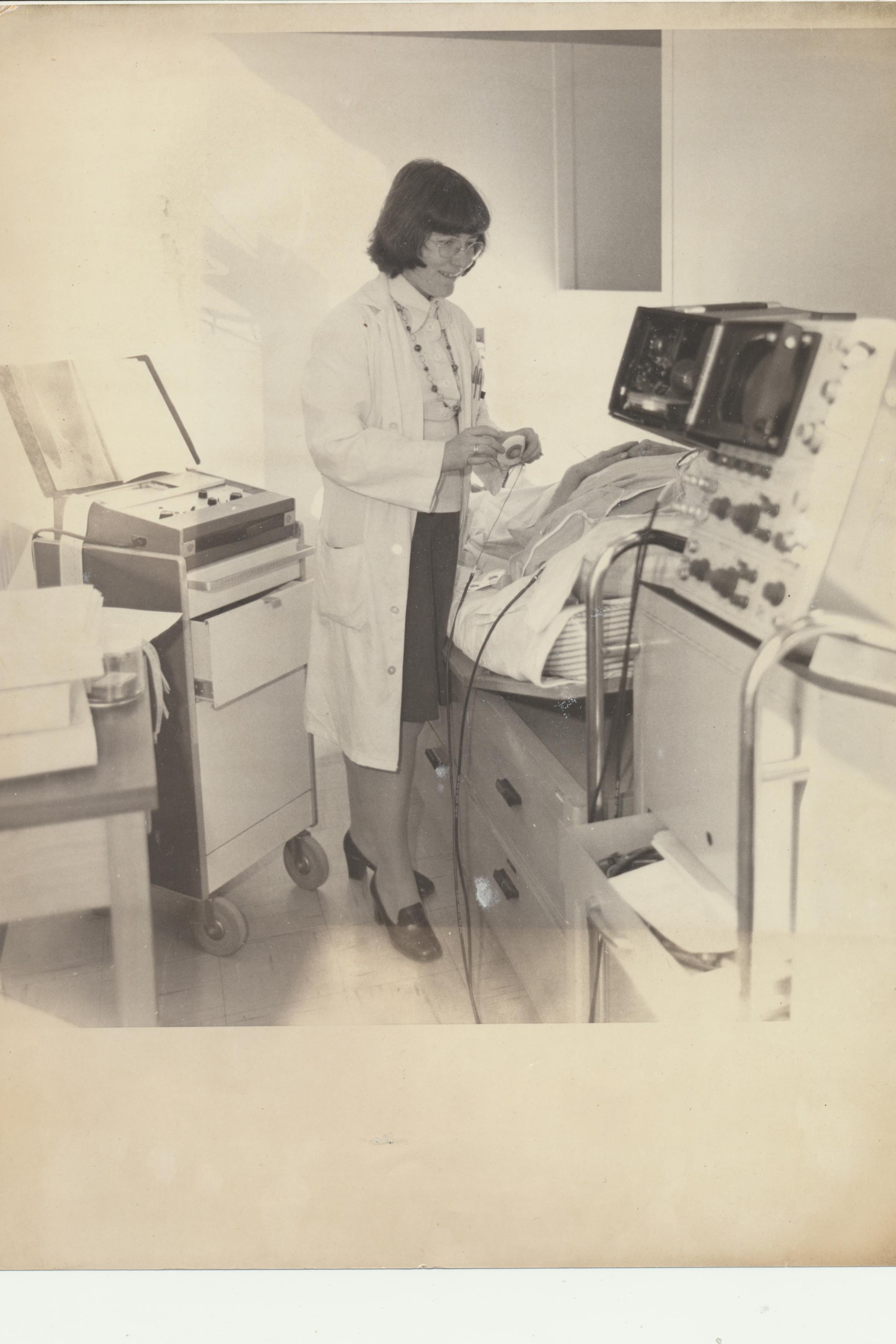 Black and white photo of Professor Frize standing in front of medical machines wearing a lab coat